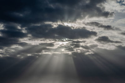 Low angle view of sunlight streaming through clouds