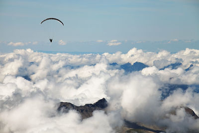 Person paragliding over cloudscape against blue sky at swiss alps