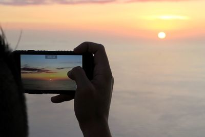 Close-up of hand using mobile phone against sky during sunset