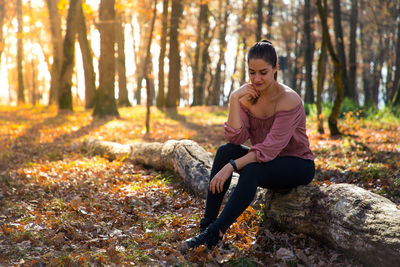 Smiling young woman sitting on fallen tree trunk in forest