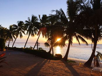 Silhouette palm trees on beach against sky during sunset