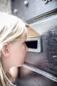 Side view of girl looking through mail slot in door