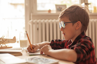 Nerdy elementary student writing his homework in the living room.