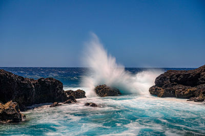 Waves splashing on rocks against clear sky