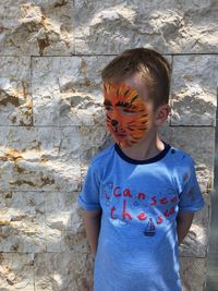 Cute boy with face paint standing against stone wall