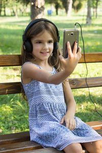 Smiling girl listening music while sitting on bench at park