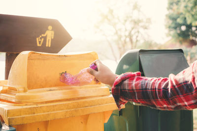 Cropped hand putting plastic water bottle in garbage bin at public park