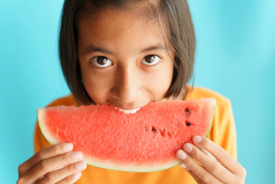Close-up portrait of girl eating watermelon against blue background
