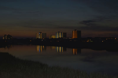 Scenic view of lake by illuminated buildings against sky at sunset