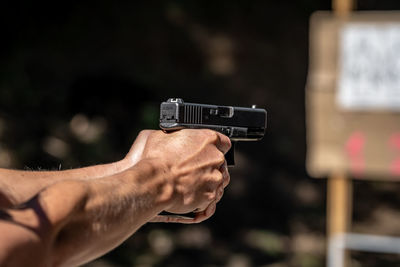 Cropped hand of man holding gun against black background