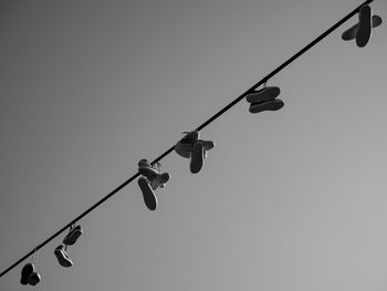 Low angle view of shoes hanging on cable against clear sky