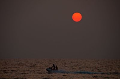 People jet boating in sea against sky during dusk