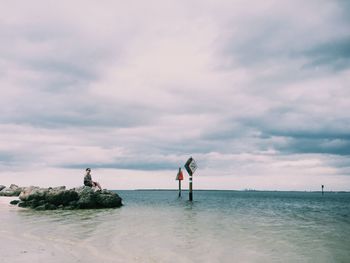 Man sitting on rock at sea against sky