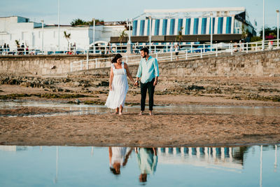 Full length of couple standing on beach against sky