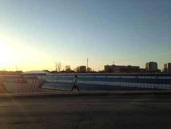 Woman walking on road against clear sky at sunset