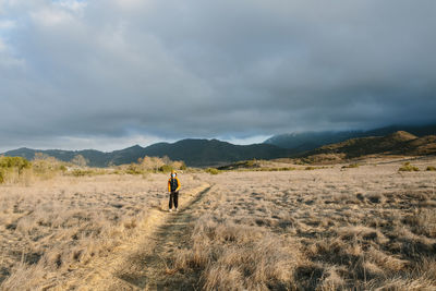 Rear view of man walking on field against sky