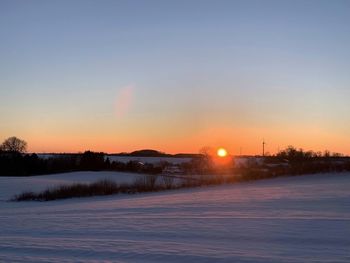 Snow covered landscape against sky during sunset