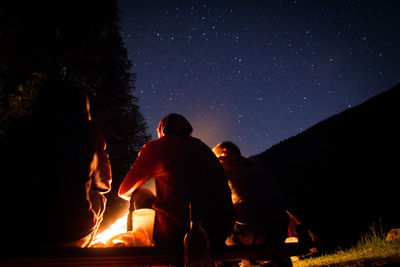 Rear view of friends sitting by campfire against star field