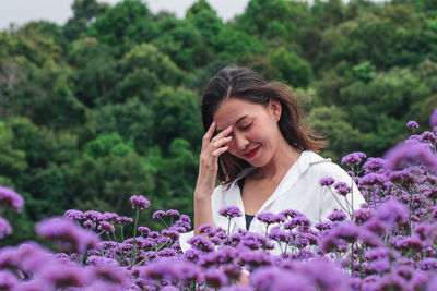 Smiling beautiful woman standing by purple flowering plants