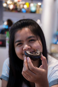 Close-up portrait of smiling young woman eating donut