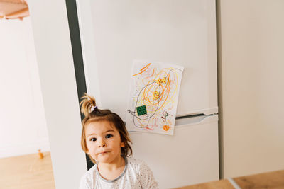 Portrait of girl by drawing on refrigerator in home