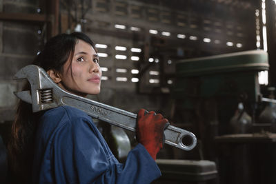 Side view of young woman with large wrench standing in factory