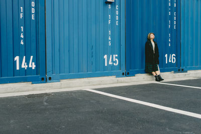 Full length of young woman leaning on cargo container