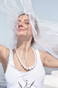 Woman with eyes closed holding scarf against sky