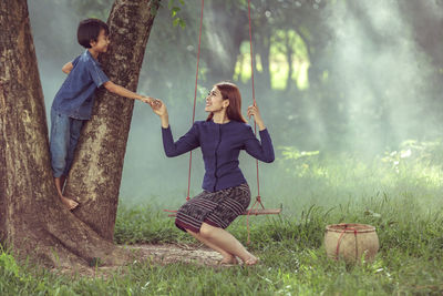 Full length of smiling young woman standing on grass against trees