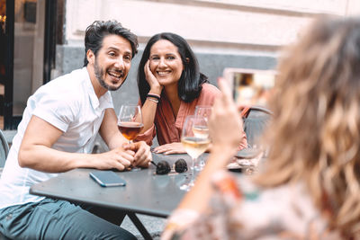 Woman photographing smiling couple at sidewalk cafe