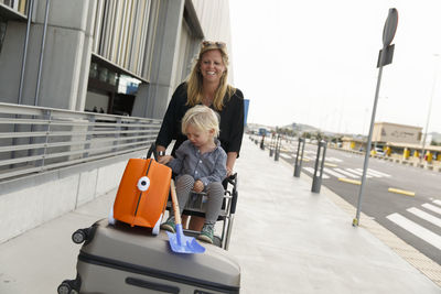 Mother pushing son sitting on luggage trolley