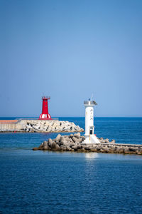 Lighthouse by sea against clear blue sky