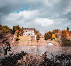 River amidst buildings and trees against sky