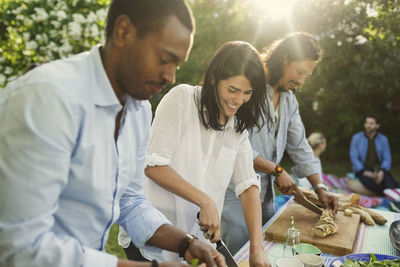 Happy young woman with male friends preparing food in backyard during summer party