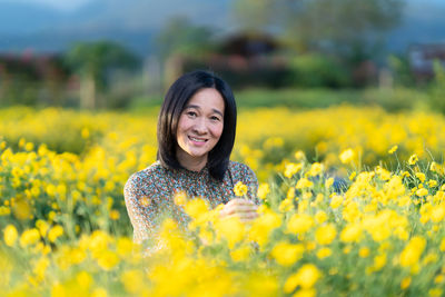 Portrait of smiling young woman with yellow flower in field