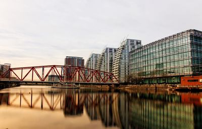 Bridge over river by buildings against sky