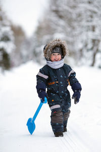 Toddler girl wearing winter clothes having fun outside in snowy day. girl is playing with shovel.