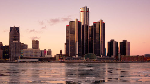 Modern buildings by frozen lake in city during sunset