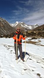 Full length of man holding sticks while standing on snow covered land against mountains and sky