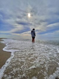 Rear view of man standing on beach against sky
