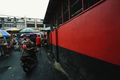 People on wet road amidst buildings in city during rainy season