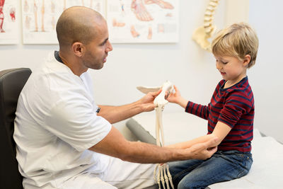 Male doctor explaining hand model to boy at orthopedic clinic