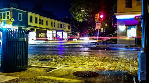 Wet road by illuminated buildings in city at night