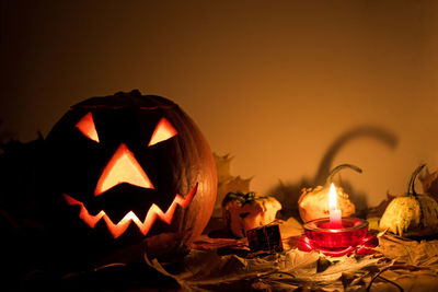 Close-up of illuminated pumpkin against orange wall during halloween