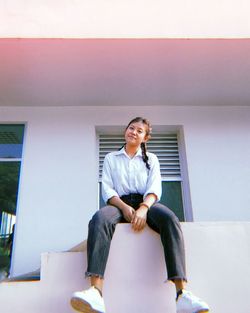 Portrait of smiling young woman sitting on wall