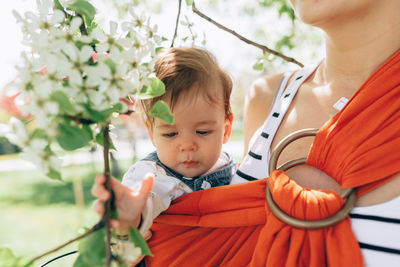 Mother holding cute girl in orange sling outdoors