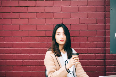 Portrait of beautiful young woman standing against brick wall