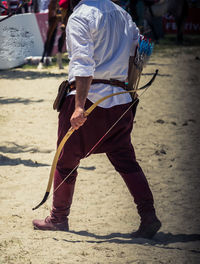 Low section of man with bow and arrow walking outdoors