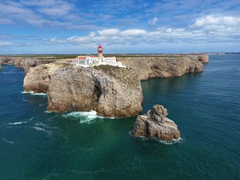 Lighthouse on rock by sea against sky