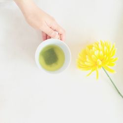 Cropped hand holding green tea cup by flower over table